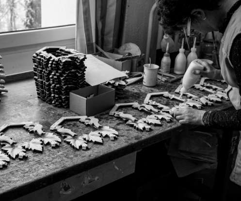 Schwarzweiß Fotografie. Dekore von Kuckucksuhr liegen auf einer Werkbank und werden verleimt.