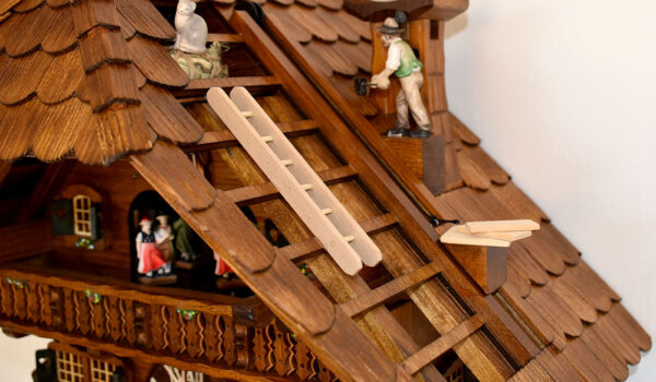 Dachdeckeruhr shows as motive a roofer on a shingled roof and a cat on the hayloft